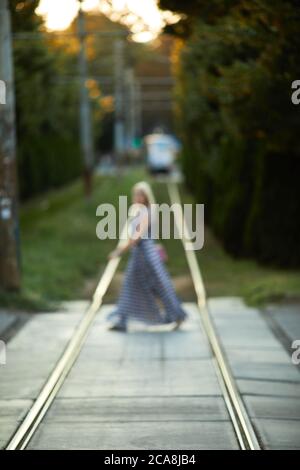 la ragazza sfocata attraversa le linee del tram in città in una giornata di sole Foto Stock