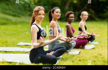 Gruppo di diverse giovani ragazze che praticano la meditazione, seduti su stuoie yoga in lotus posa all'aperto, spazio copia Foto Stock