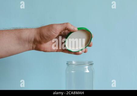 La mano chiude un vaso di vetro vuoto con un coperchio verde metallico. Mano dell'uomo su un vaso di vetro. Uomo di razza europea di mezza età. Confezionamento alimentare Foto Stock