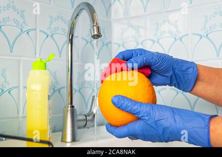 La persona lava la frutta con sapone ecologico per il lavaggio in una cucina con pareti blu. Decontaminazione e disinfezione dei prodotti dal punto vendita. Prevenzione di Foto Stock