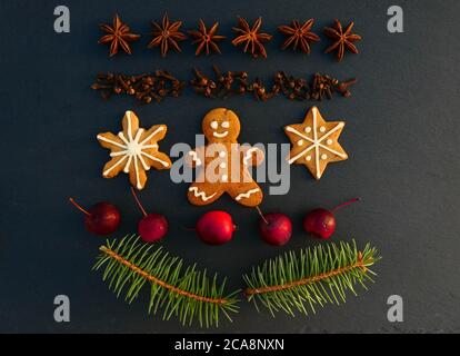 Sfondo della decorazione di Natale con biscotti di pan di zenzero. Rami di abete rosso, spezie e mele su tavola di pietra nera. Foto Stock
