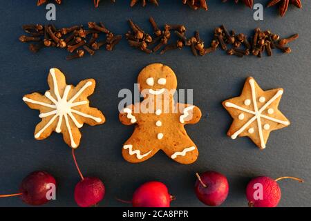 Sfondo decorazione di Natale con pan di zenzero uomo e biscotti stelle. Spezie e mele su tavola di pietra nera. Foto Stock