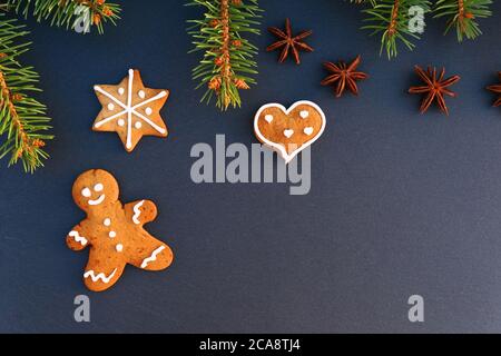 Bordo di Natale fatto di ramo dell'albero dell'abete rosso, biscotti dell'uomo del pan di zenzero su sfondo scuro della tavola di pietra. Foto Stock