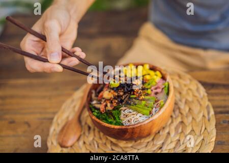 Uomo che mangia ciotola di poke con gamberi, mais, avocado, zenzero e funghi Foto Stock