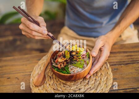 Uomo che mangia ciotola di poke con gamberi, mais, avocado, zenzero e funghi Foto Stock