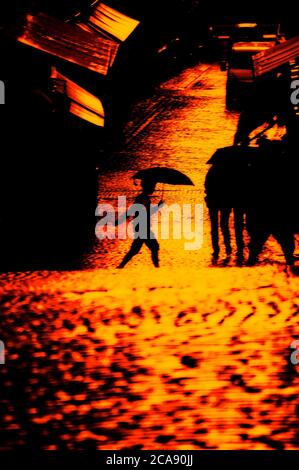 Silhouette di un ragazzo con un ombrello che scorre lungo una strada acciottolata a Stoccolma Foto Stock