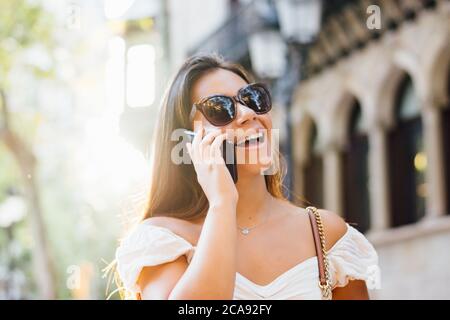 donna con occhiali da sole parla al telefono intorno alla città Foto Stock