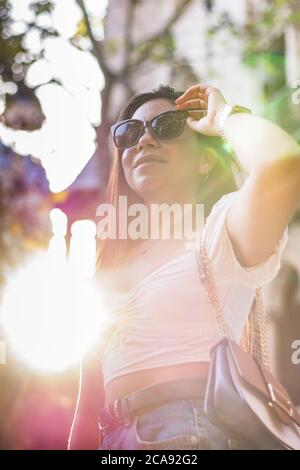 donna con occhiali da sole sorride mentre cammina per la città Foto Stock