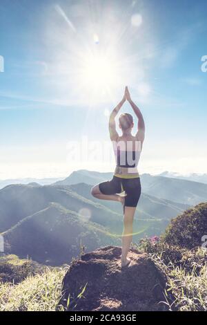 Una giovane donna in piedi su una montagna nella foresta pluviale, in una posa yoga, fotografata contro la luce del sole, Brasile, Sud America Foto Stock