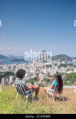 Una coppia multietnica che si siede insieme e si affaccia sul Pan di zucchero e sullo skyline di Rio, Rio de Janeiro, Brasile, Sud America Foto Stock