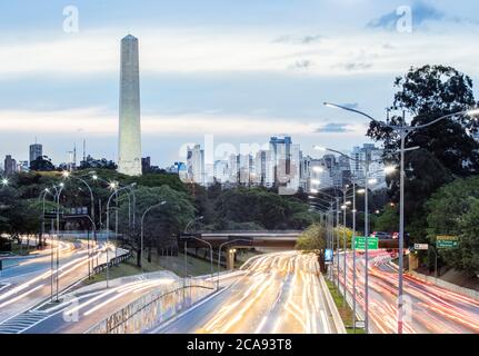 I sentieri del semaforo dell'ora di punta su 23 de Maio Avenue, lo skyline e l'Obelisco degli Eroi nel Parco Ibirapuera, San Paolo, Brasile, Sud America Foto Stock