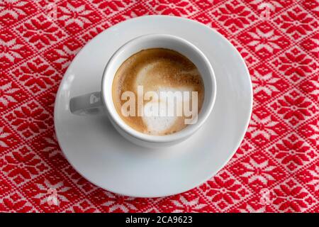 Tazza bianca di caffè con schiuma e bolle su una tovaglia rossa Foto Stock