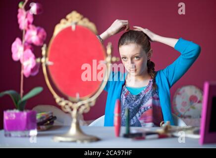 Giovane ragazzina di quattordici anni si siede nella sua camera da letto che compone in uno specchio sulla sua tabella di vestizione in preparazione per uscire. Foto Stock