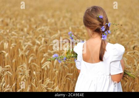 Bambina con un bouquet di fiori selvatici nelle mani in un campo di grano. Foto Stock