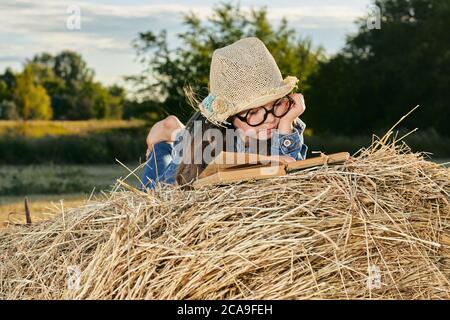 La ragazza di lettura si siede sopra il rullo del haystack sul campo in campagna. Foto di alta qualità Foto Stock