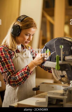 il carpentiere caucasico guida una sega circolare, lavoro concentrato della donna in fabbrica contrario a opinione che questo è un lavoro dell'uomo. il concetto di femminismo Foto Stock