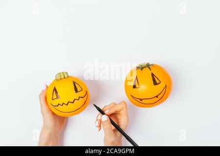 Le mani della donna disegnano facce divertenti sulle zucche, preparandosi per la celebrazione di Halloween. Foto Stock