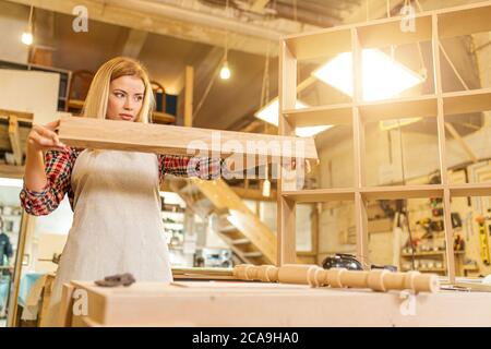 lavoratrice dura donna che controlla pezzo di legno, donna fa mobili fatti a mano in officina Foto Stock
