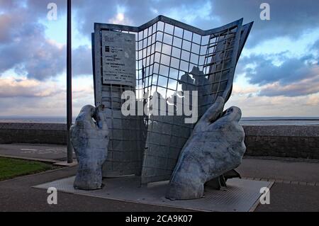 Un'opera d'arte di due mani che tiene un giornale simile a una griglia sul lungomare di Minehead Foto Stock