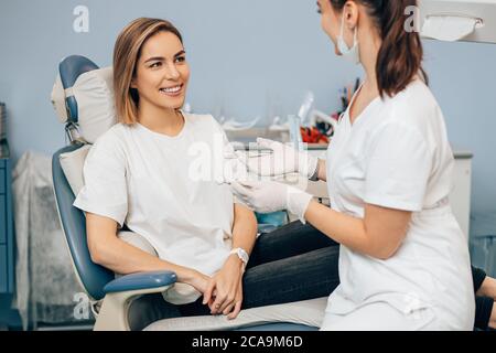 donna dentista amichevole trattando bella paziente in studio dentistico, medico in uniforme bianca, ortodontista professionale Foto Stock