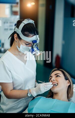 giovane dentista medico in uniforme bianca e speciale lampada fronte esaminare i denti del paziente, liberandosi di denti rovinati Foto Stock