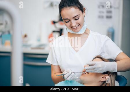 dentista professionista attento in uniforme bianca trattando i denti del paziente, facendo sorriso perfetto per i pazienti, utilizzando apparecchiature mediche Foto Stock