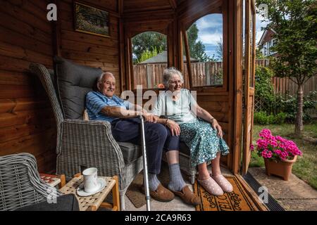 Coppie anziane negli anni 80 che si godono il caldo clima estivo nella loro casa estiva giardino, Inghilterra, Regno Unito Foto Stock