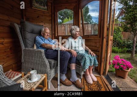 Coppie anziane negli anni 80 che si godono il caldo clima estivo nella loro casa estiva giardino, Inghilterra, Regno Unito Foto Stock