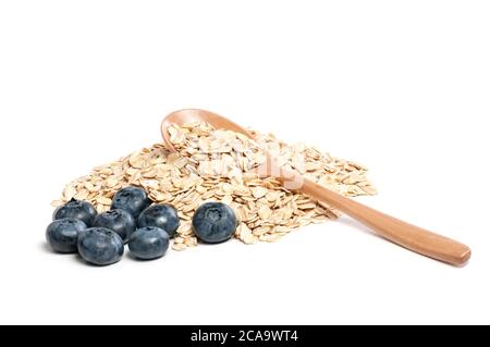 Pila di fiocchi d'avena grezzi con il cucchiaio di legno con i mirtilli freschi isolati su bianco. Macro ad alta risoluzione in primo piano di farina d'avena. Foto Stock