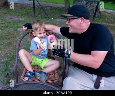 Padre e figlio tostano insieme i coni di gelato in un patio esterno. Rzeczyca Polonia Centrale Europa Foto Stock