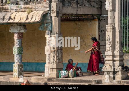 Mayiladuthurai, Tamil Nadu, India - Febbraio 2020: Due donne indiane in sari rossi con le colonne ornately intagliate dell'antico tempio indù a Vaith Foto Stock