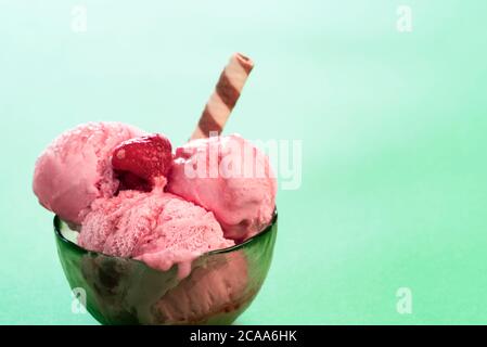 Ciotola di gelato al lampone con sciroppo, isolata su fondo verde menta. Primo piano di gelato con frutti di bosco. Dessert surgelato fatto in casa. Foto Stock
