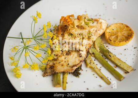 Un filetto di branzino pescato in linea, il labrax Dicentrarchus, fritto in burro che è stato servito su una fetta di finocchio e aromatizzato con limone e selvatico Foto Stock