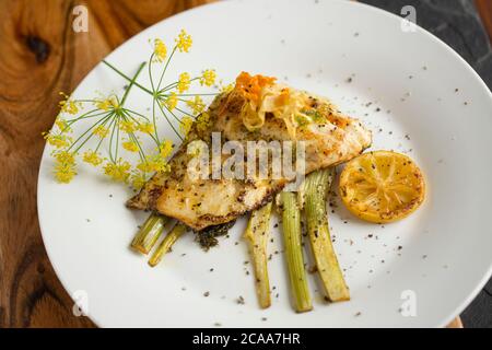 Un filetto di branzino pescato in linea, il labrax Dicentrarchus, fritto in burro che è stato servito su una fetta di finocchio e aromatizzato con limone e selvatico Foto Stock