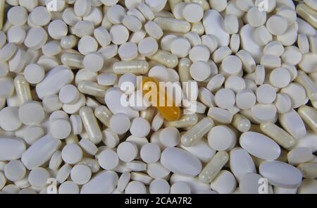 Closeup full frame di pile innumerevoli pillole bianche e capsule con una capsula gialla al centro (concentrarsi sulla pillola gialla) Foto Stock