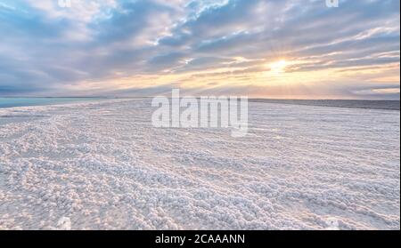 Spiaggia cristallina di sale bianco illuminata dal sole del mattino, piccole pozzanghere con acqua di mare al Mar Morto - il lago più iperialino del mondo Foto Stock