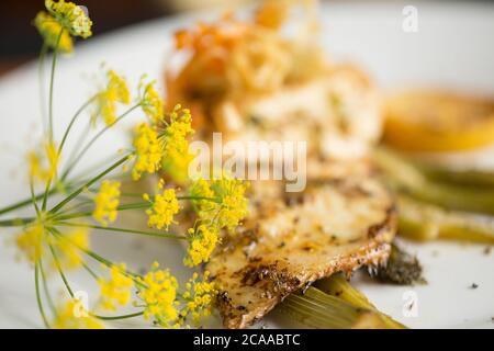 Un filetto di branzino pescato in linea, il labrax Dicentrarchus, fritto in burro che è stato servito su una fetta di finocchio e aromatizzato con limone e selvatico Foto Stock