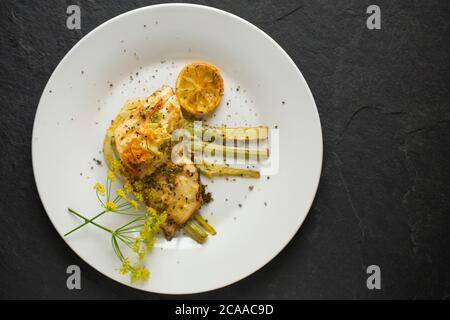 Un filetto di branzino pescato in linea, il labrax Dicentrarchus, fritto in burro che è stato servito su una fetta di finocchio e aromatizzato con limone e selvatico Foto Stock