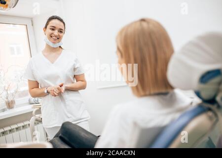 donna dentista amichevole trattando bella paziente in studio dentistico, medico in uniforme bianca, ortodontista professionale Foto Stock