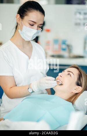 Giovane dentista femminile alla ricerca di denti viziati, paziente vuole avere un sorriso perfetto, un trattamento attento da parte di un medico professionista Foto Stock