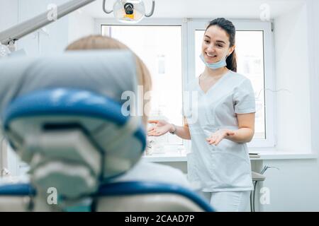 giovane donna caucasica siediti litlen alle raccomandazioni del medico prima del trattamento dei denti, sorridendo femmina caucasica in camera dentista Foto Stock