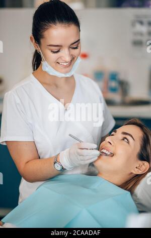 donna dentista amichevole trattando bella paziente in studio dentistico, medico in uniforme bianca, ortodontista professionale Foto Stock