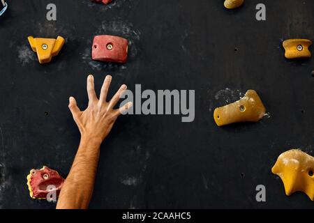 Macro shot degli scalatori mani coperte con magnesio chalk, afferrando le maniglie colorate nel corso arrampicata indoor allenamento Foto Stock