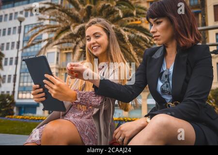 Ripresa orizzontale di due giovani imprenditrici che parlano e guardano al tablet fuori dell'ufficio Foto Stock