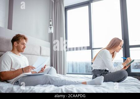 giovane bell'uomo dai capelli giusti che pensa alla sua attività mentre sua moglie sta leggendo un libro. vista laterale foto. lavoro di cervello. uomo che fa le storie in Foto Stock