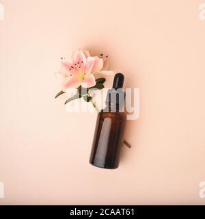 Bottiglia di siero di vetro con pipetta e fiore bello su sfondo rosa beige. Natural Organic Spa concetto cosmetico. Vista frontale. Foto Stock