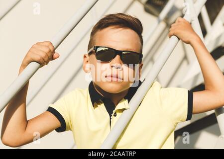 Ragazzo asiatico in una t-shirt gialla si siede sulle scale indossando occhiali da sole Foto Stock