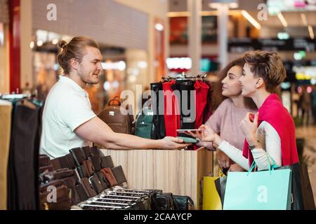 Femmina di pagamento del cliente per i prodotti in cuoio con credito contactless card con tecnologia NFC.Vendite persona con un lettore di carte di credito la macchina a un contatore Foto Stock