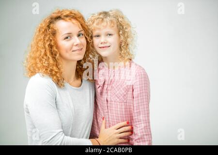 famiglia composta da una bella giovane madre dai capelli rossi e la sua bella figlia bionda, isolata su sfondo grigio. copia spazio , amore concetto Foto Stock