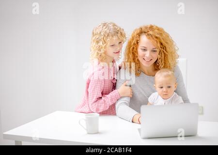 Donna zenzero e i suoi figli dai capelli lonesti che scelgono i mobili per la camera da letto. Famiglia che scarica musica da Internet. Primo piano foto Foto Stock